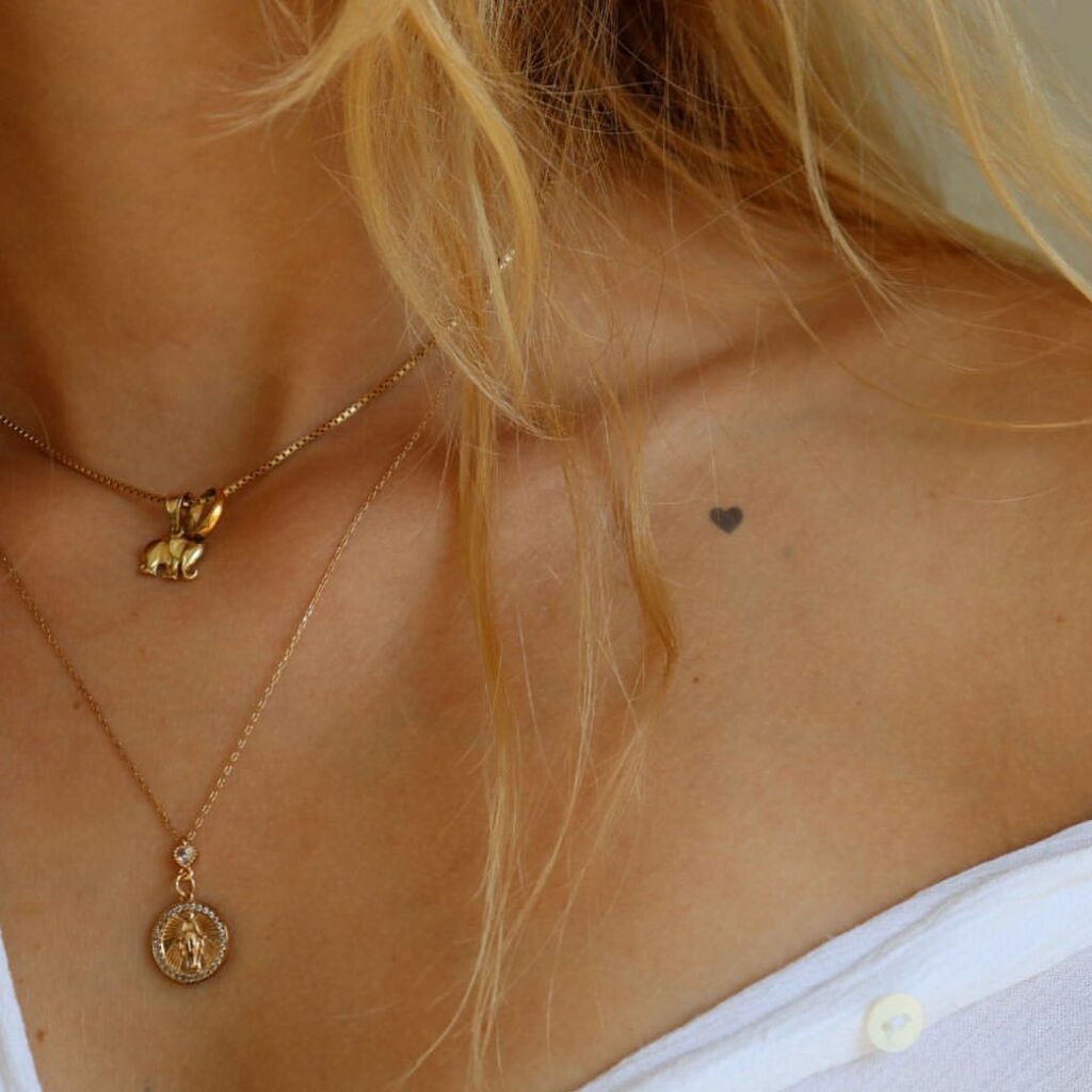 Small black filled heart tattoo nestled on the collarbone for subtle elegance tiny heartbeat