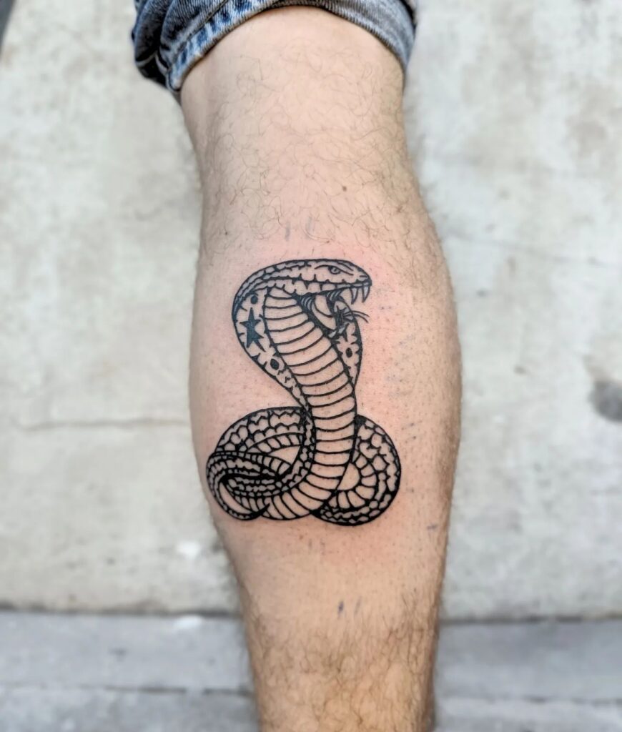 Small black work cobra tattoo on the calf, capturing the cobra in a coiled stance: coiled command