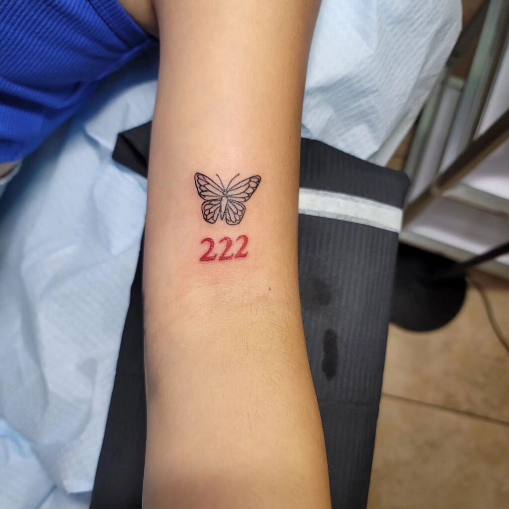 Small Butterfly with Red Color 222 Text Tattoo Above the Elbow: Colorful Contrast, a Vibrant Composition 