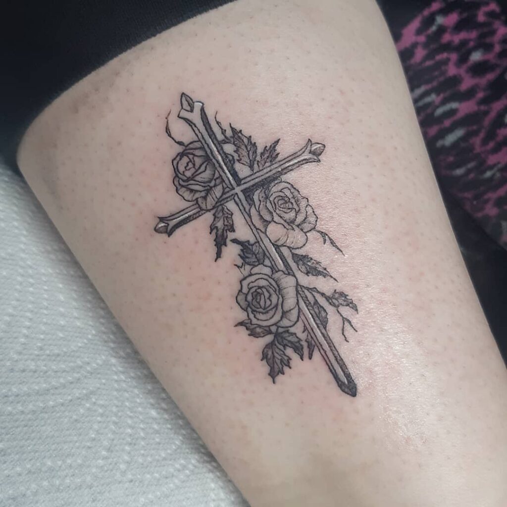 Small cross with roses above the knee or on the thigh for women a delicate and meaningful tattoo