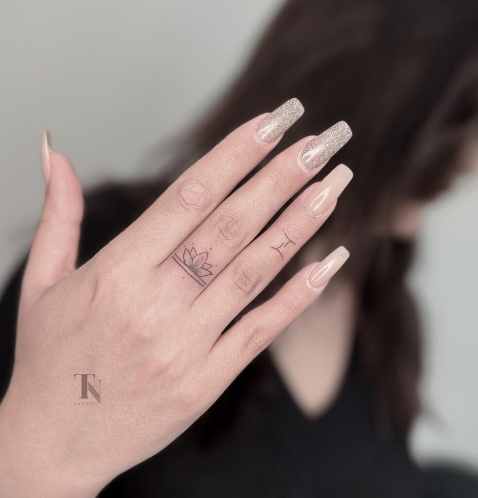 Small lotus tattoo on the middle finger, outlined with dots above lotus whispers