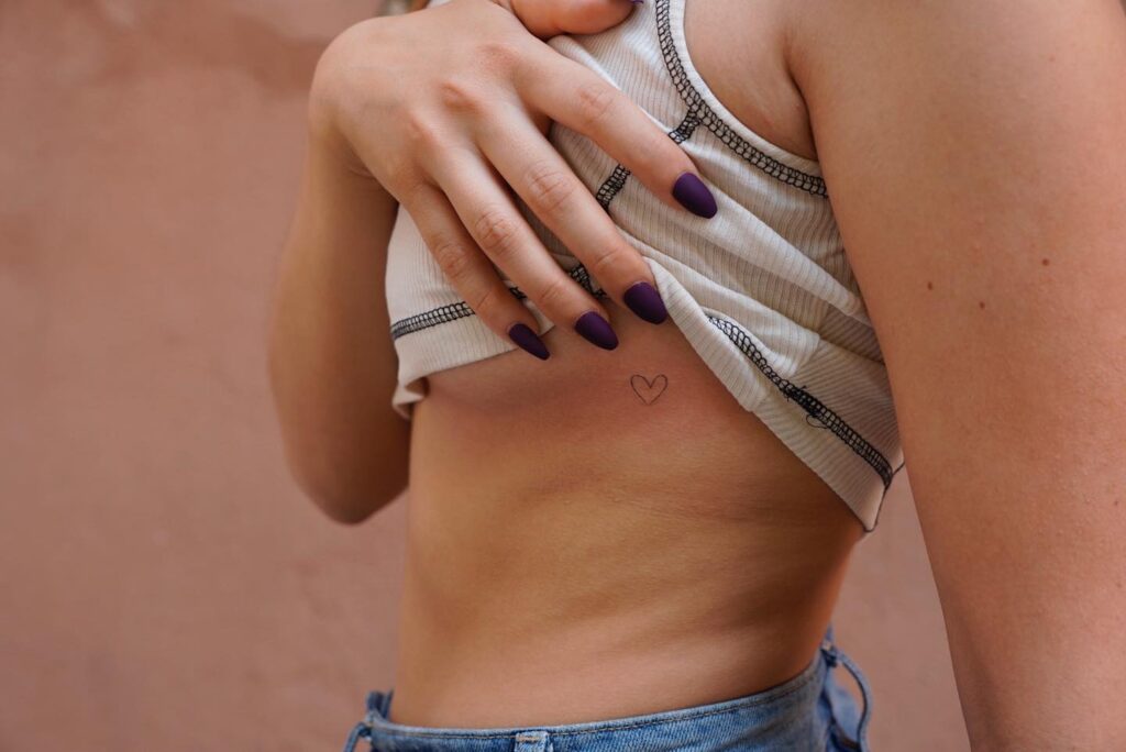 Small outline heart fineline tattoo on the rib, a dainty symbol of love double heartbeat
