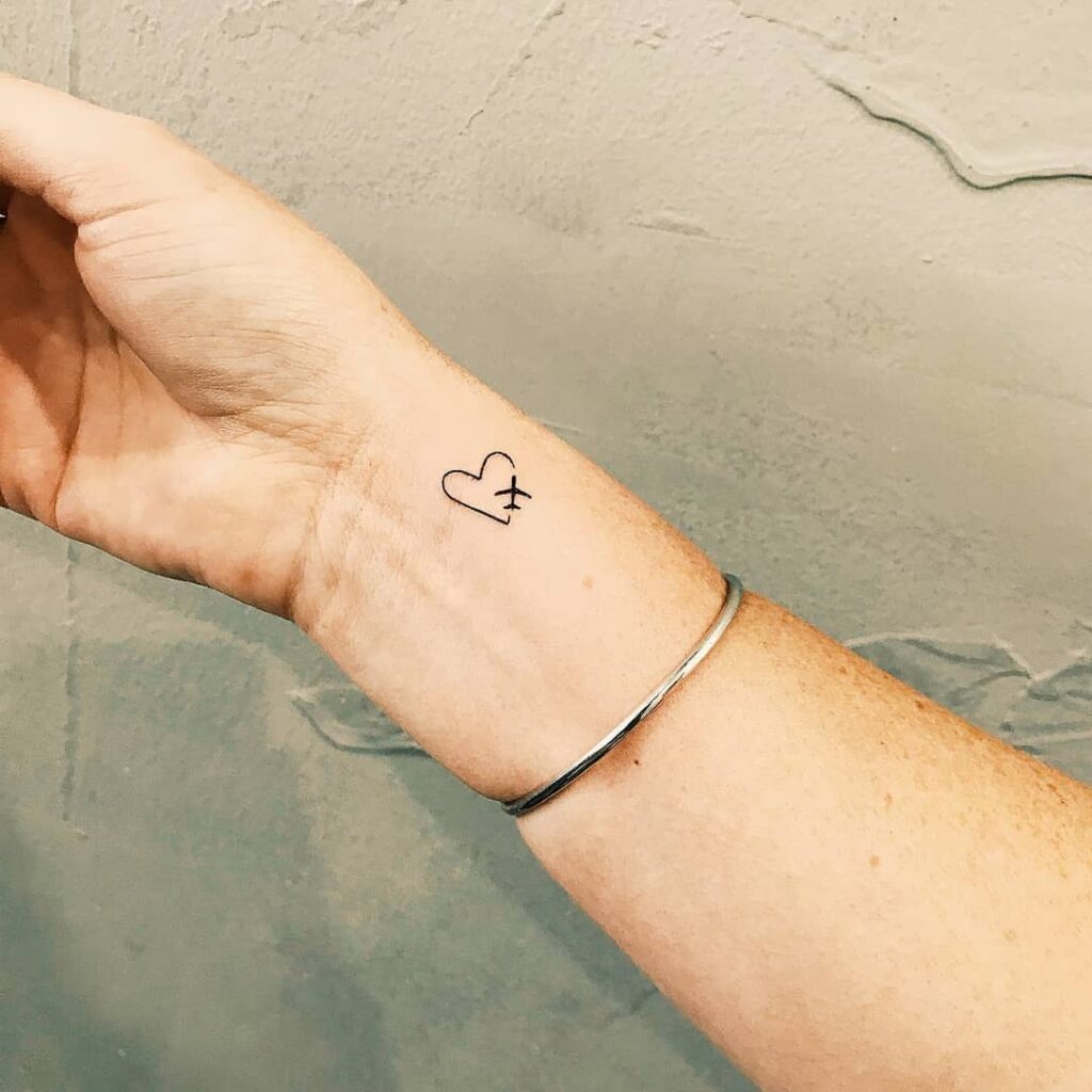 Small outline heart tattoo closed by an airplane symbol on the wrist