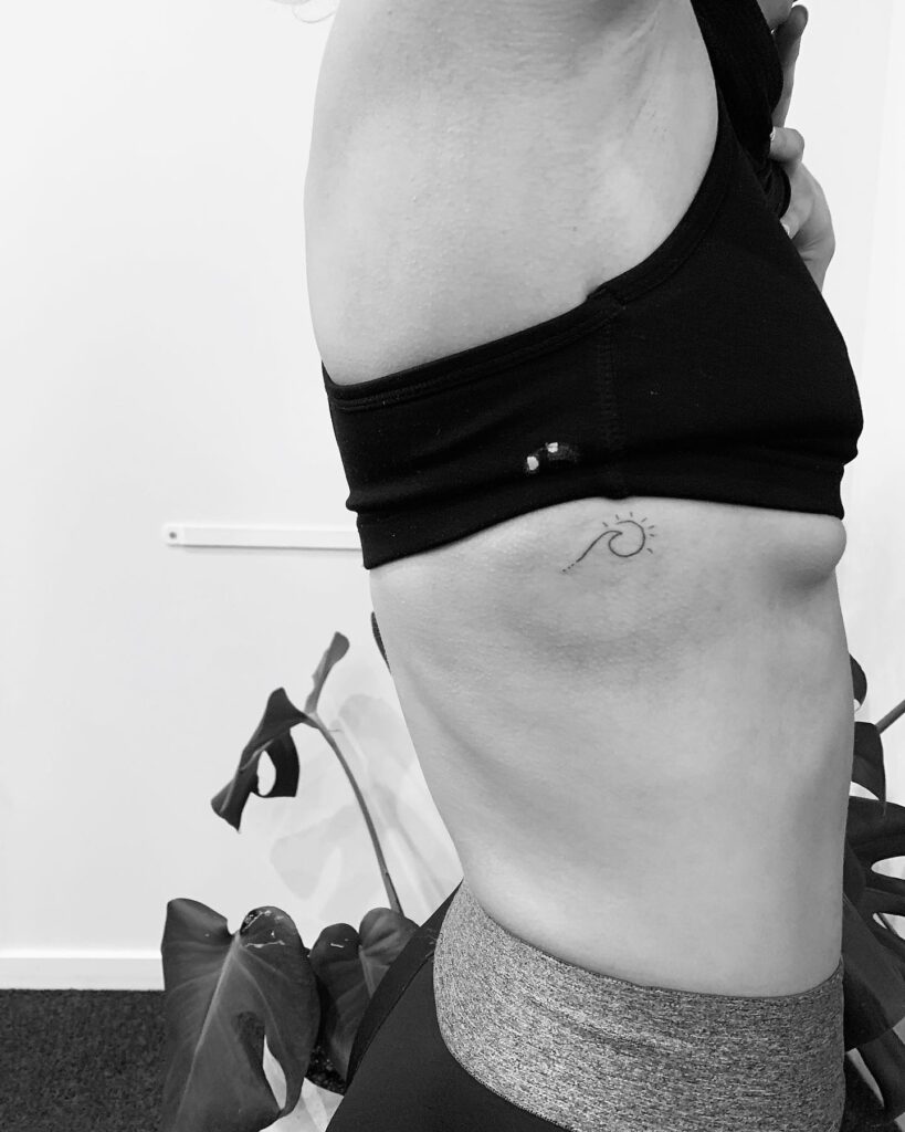 Small sun and wave tattoo on the rib: minimalistic ocean-inspired rib ink