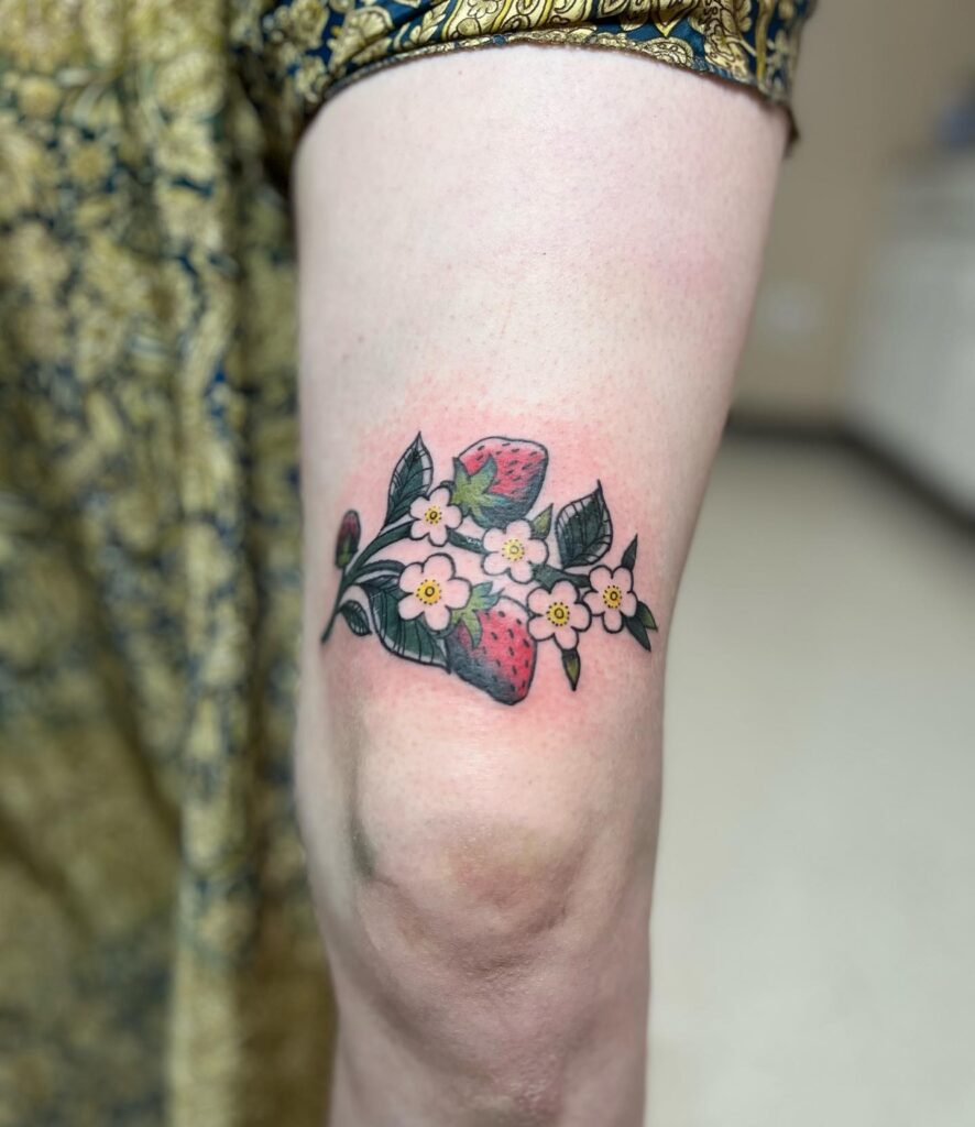 Strawberry delight above the knee tattoo with flowers