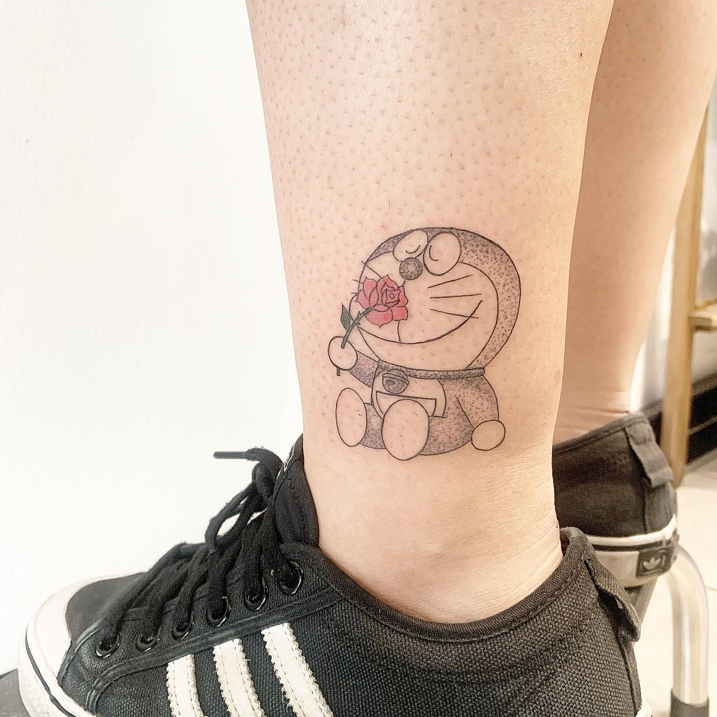 Subtle and nostalgic Doraemon holding a rose tattoo with delicate dot shading, ideal for anime lovers who appreciate vintage aesthetic ink