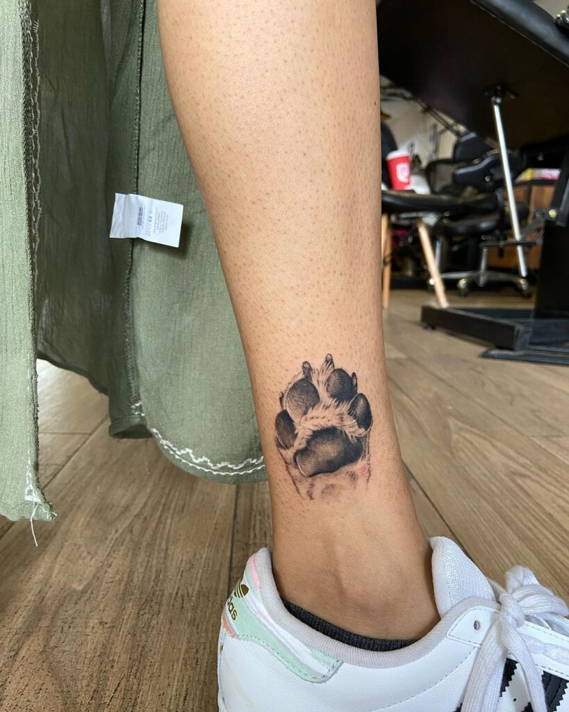 Subtle realism dog paw tattoo above the ankle for females