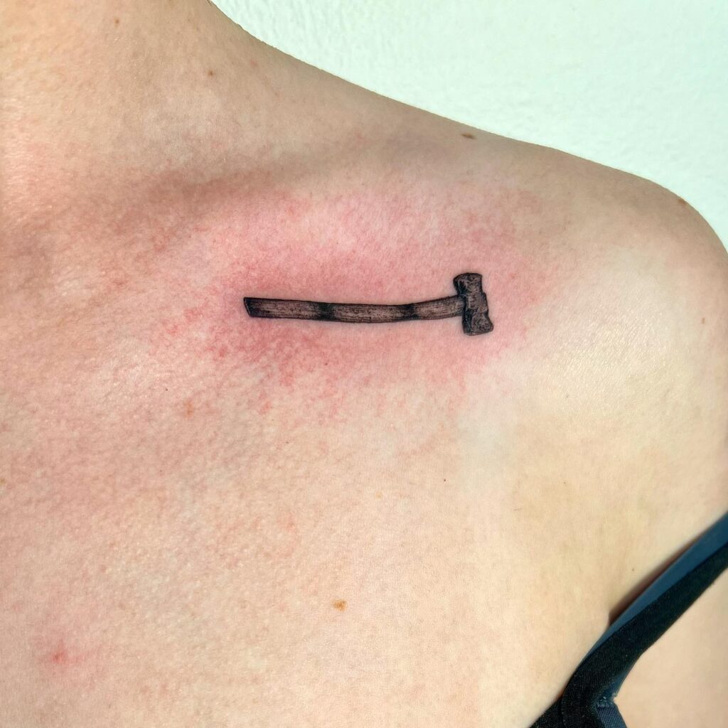 Super tiny hammer tattoo on the collarbone, a miniature emblem of power tool of strength
