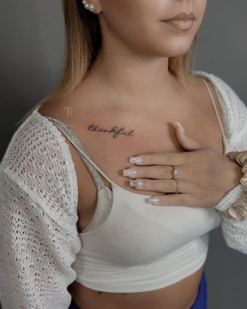 'Thankful' script lettering calligraphy tattoo on the collarbone, an expression of appreciation gratitude reminder