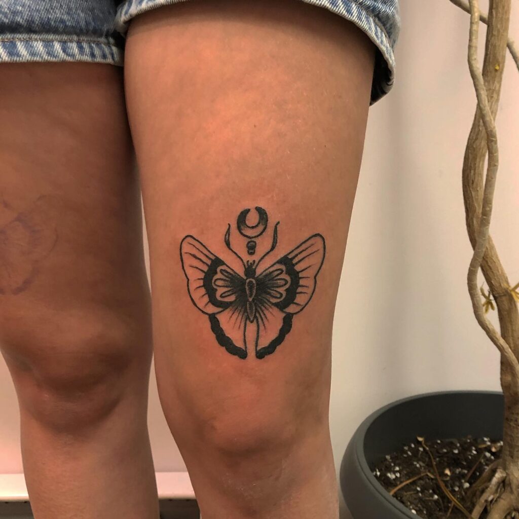 The Butterfly Design Tattoo With a Holding Crescent Object on the Thigh