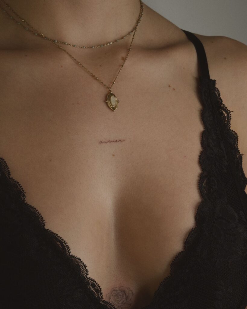 Thin 'aimer' tattoo in cute and elegant font at the middle of the collarbone aiming for grace