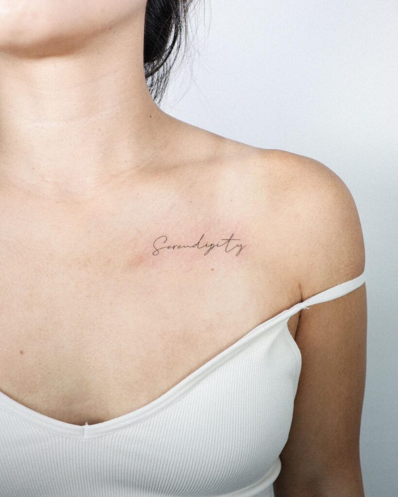 Thin line 'serendipity' word lettering tattoo on the collarbone, an elegant serendipitous reminder serendipitous charm