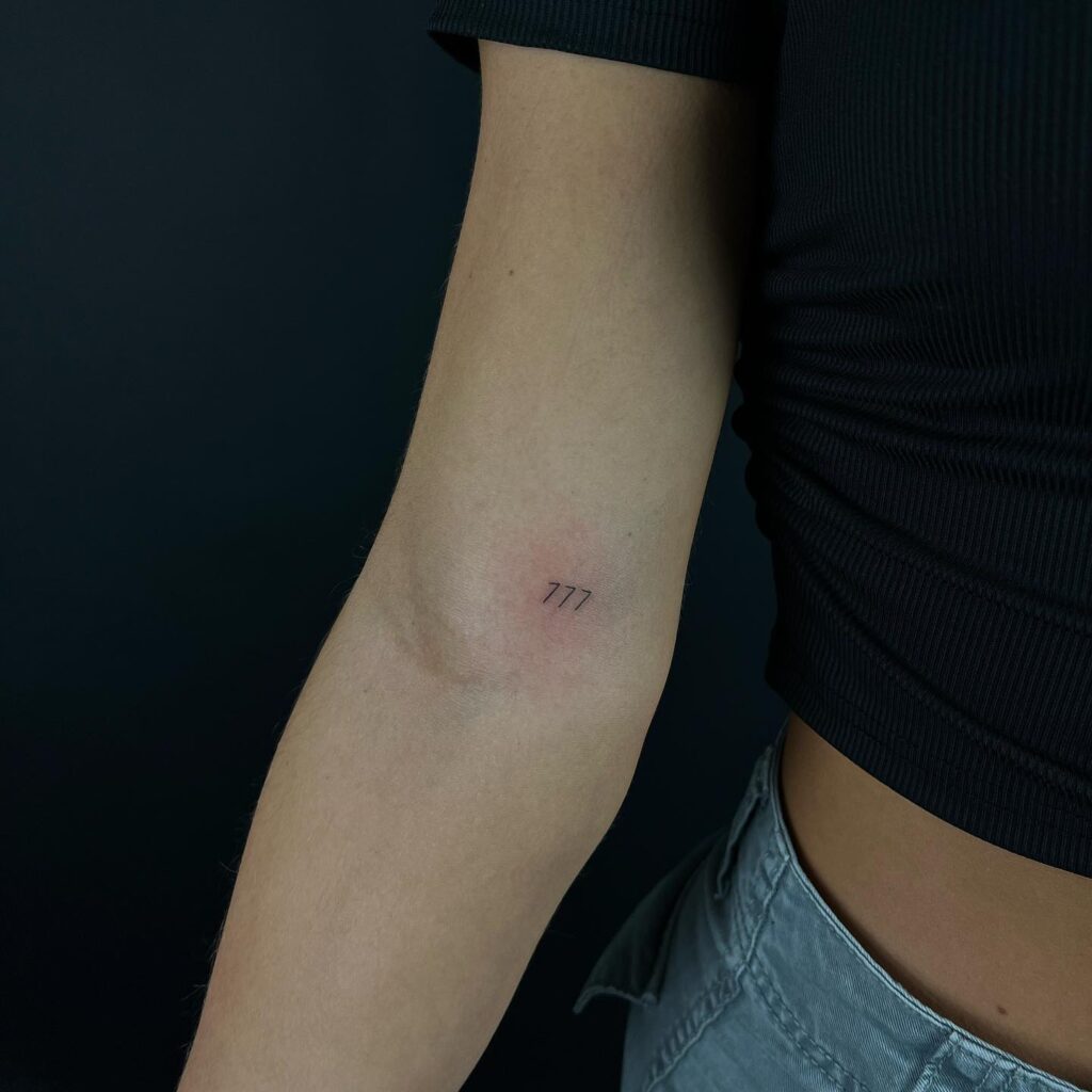 Tiny Fineline 777 Tattoo Above the Elbow: Subtle Luck 