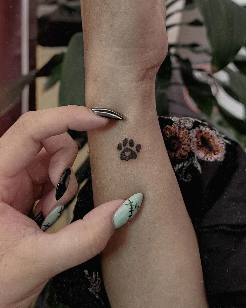 Tiny heart accent small black dog paw tattoo on the side of the wrist