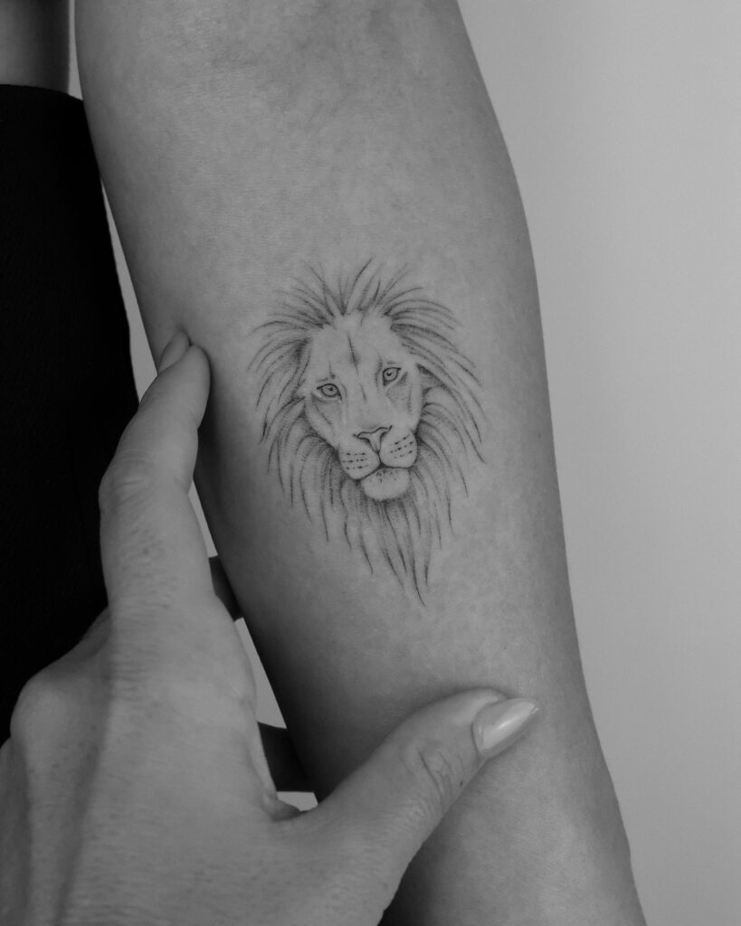 Tiny lion face tattoo on the forearm, executed in fineline for a subtle and elegant expression delicate power