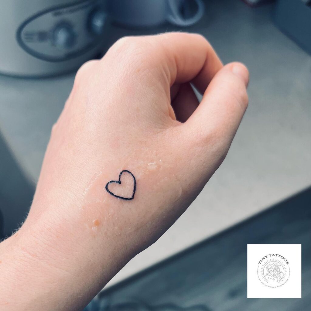 Tiny outline love heart tattoo on hand in black color
