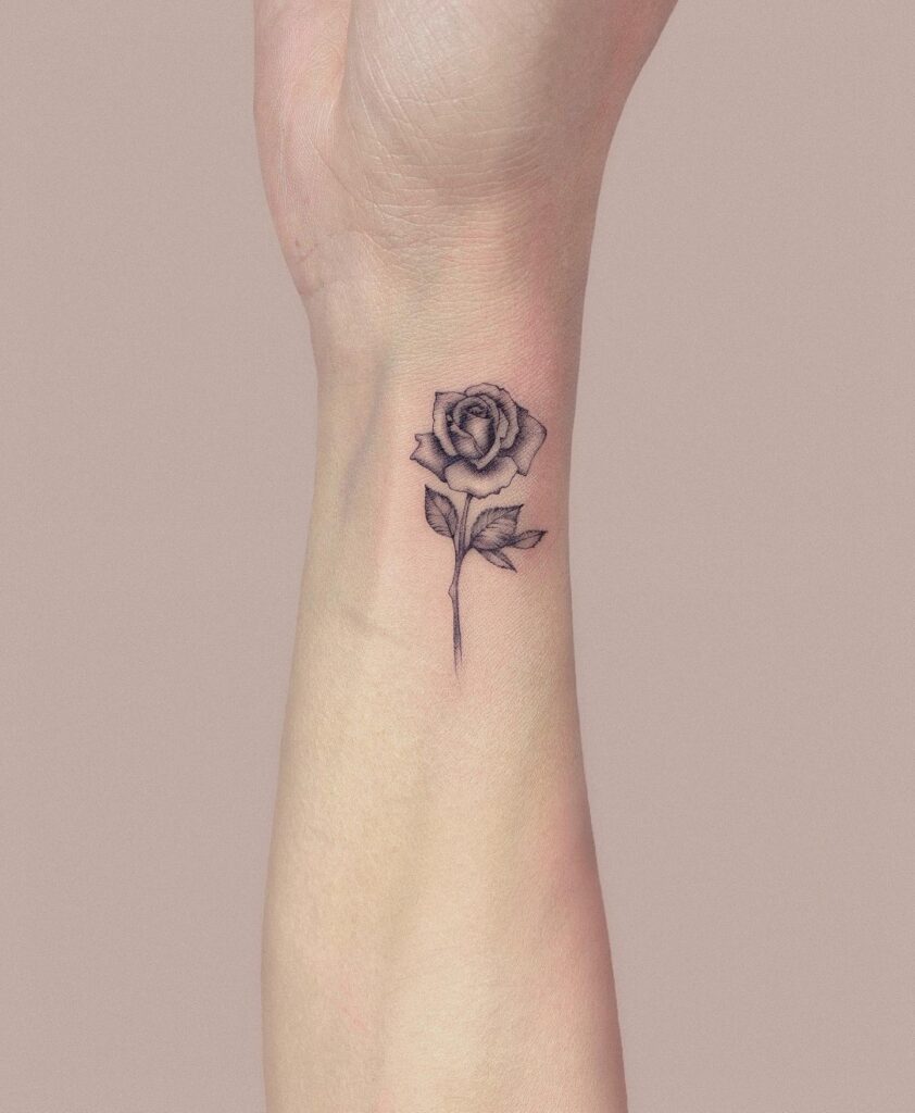 Tiny rose plant tattoo on the side wrist with realistic black and grey shading, embracing natures beauty: botanical whispers