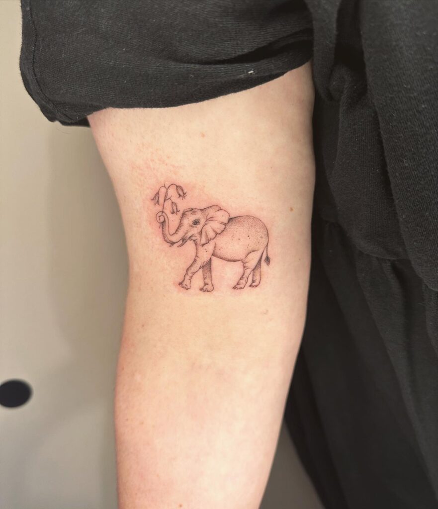 Tiny Side View Elephant Tattoo Lifting Trunk and Holding Flowers: Elbow Elegance
