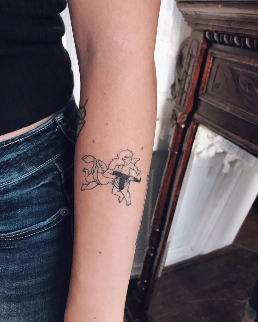 Two angels tattoo one with a gun, the other guiding - side of the forearm masterpiece