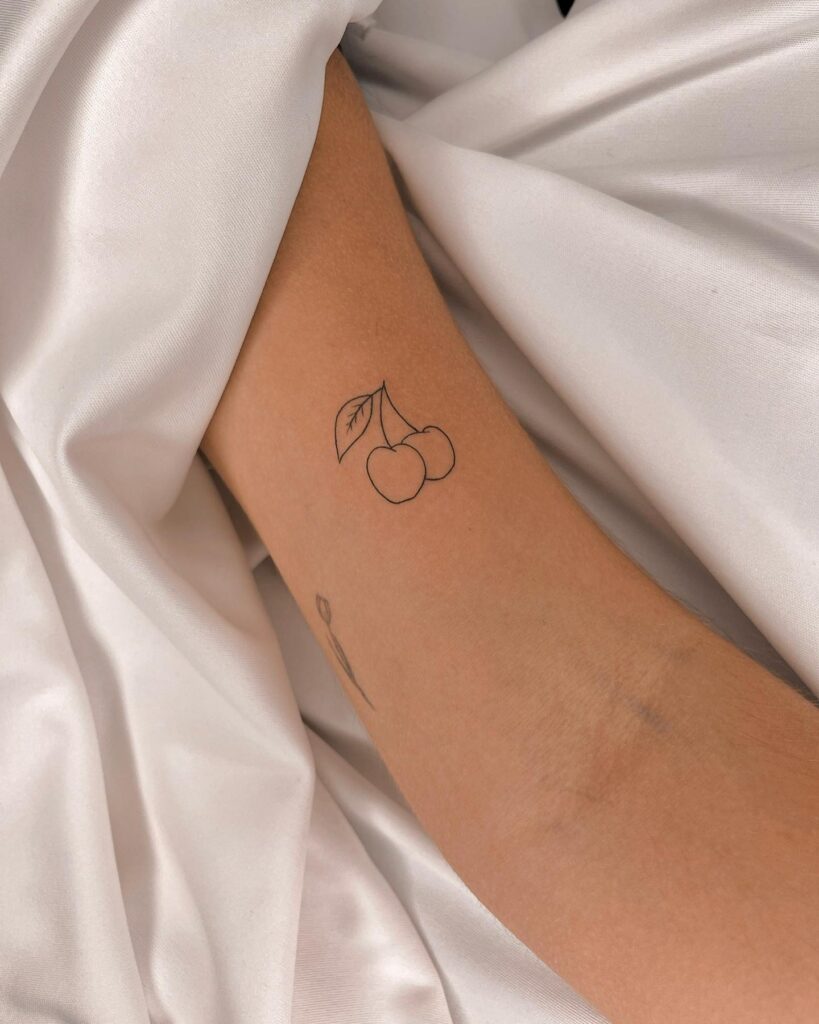 Two cherries tattoo outline on the inner bicep with a single leaf, elegant and playful: cherry duo