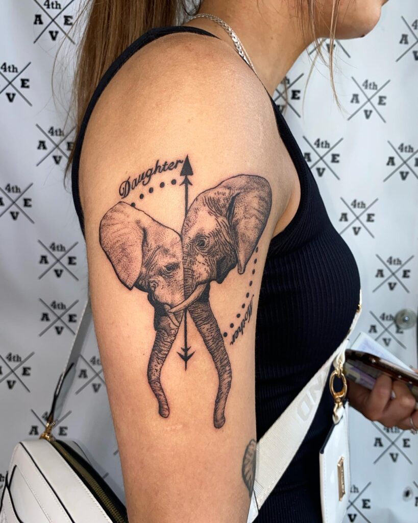 Upper arm tattoo with mother-daughter elephants: arrow-guided love