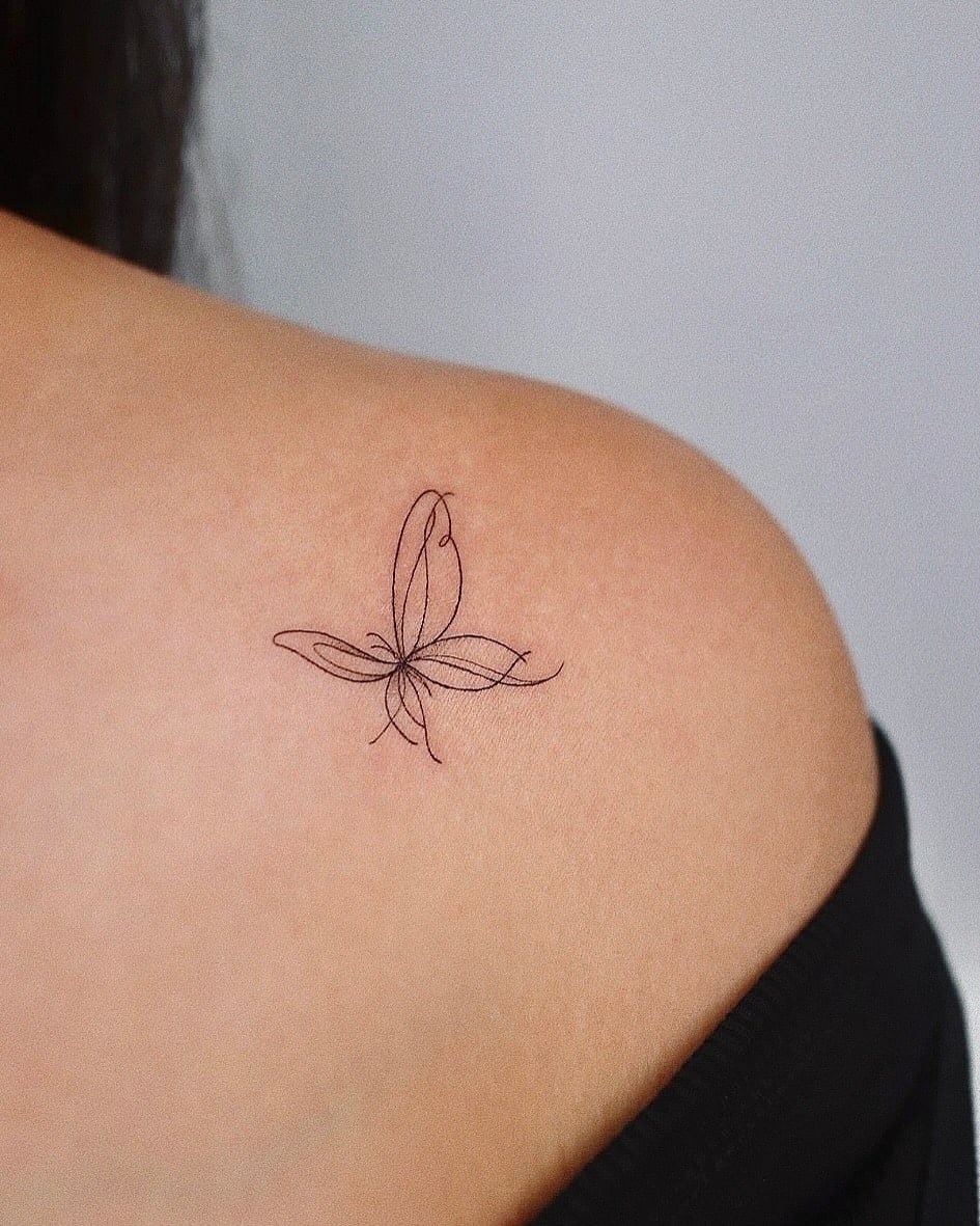 Upper shoulder collarbone butterfly tattoo with flowing minimalist lines