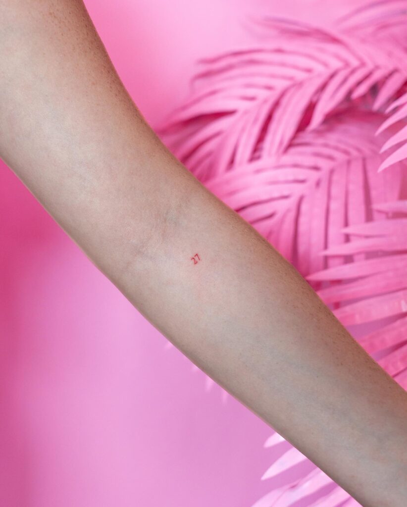Very small '27' number tattoo below the elbow on the forearm numerical whisper