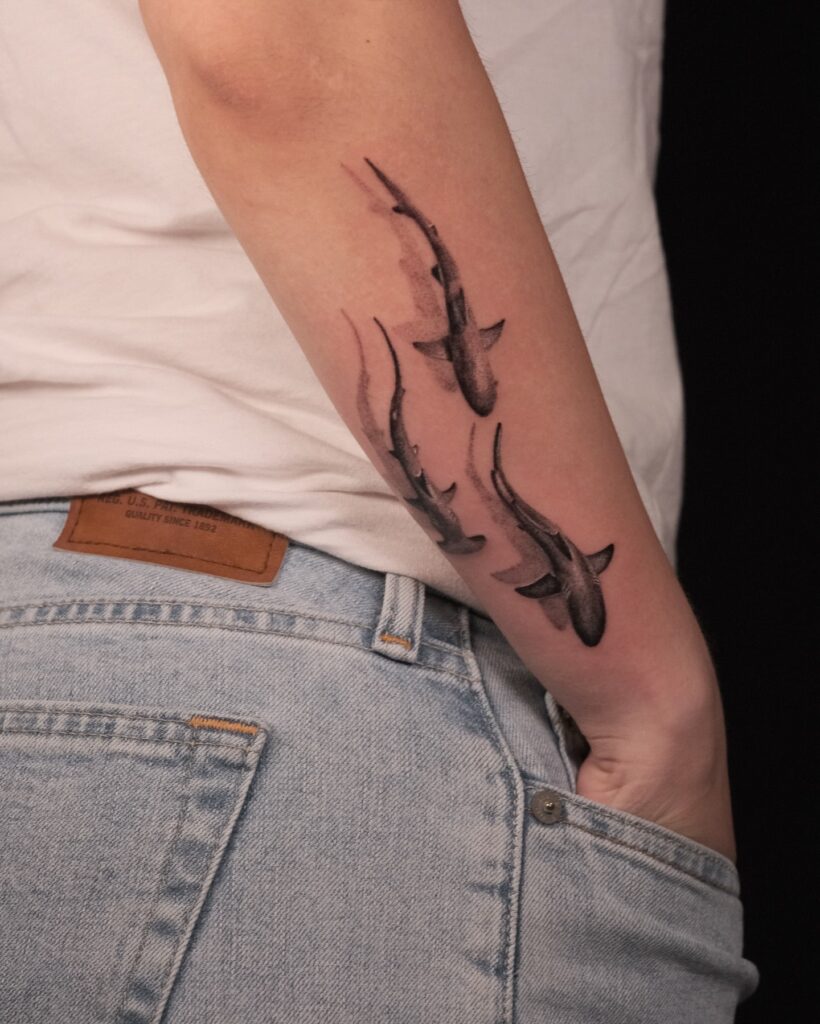 Watercolor shark trio tattoo on forearm representing movement, freedom, and a deep connection to the sea