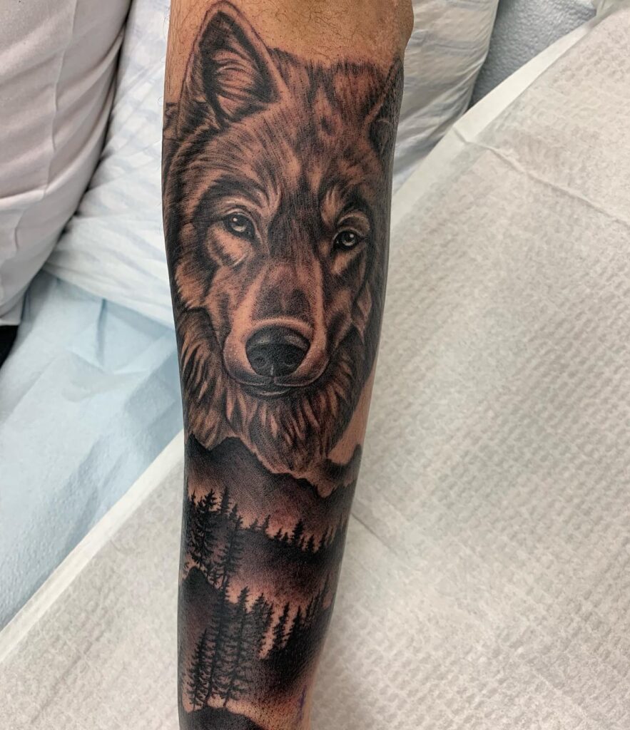 Wolf tattoo on outer forearm with majestic mountain backdrop