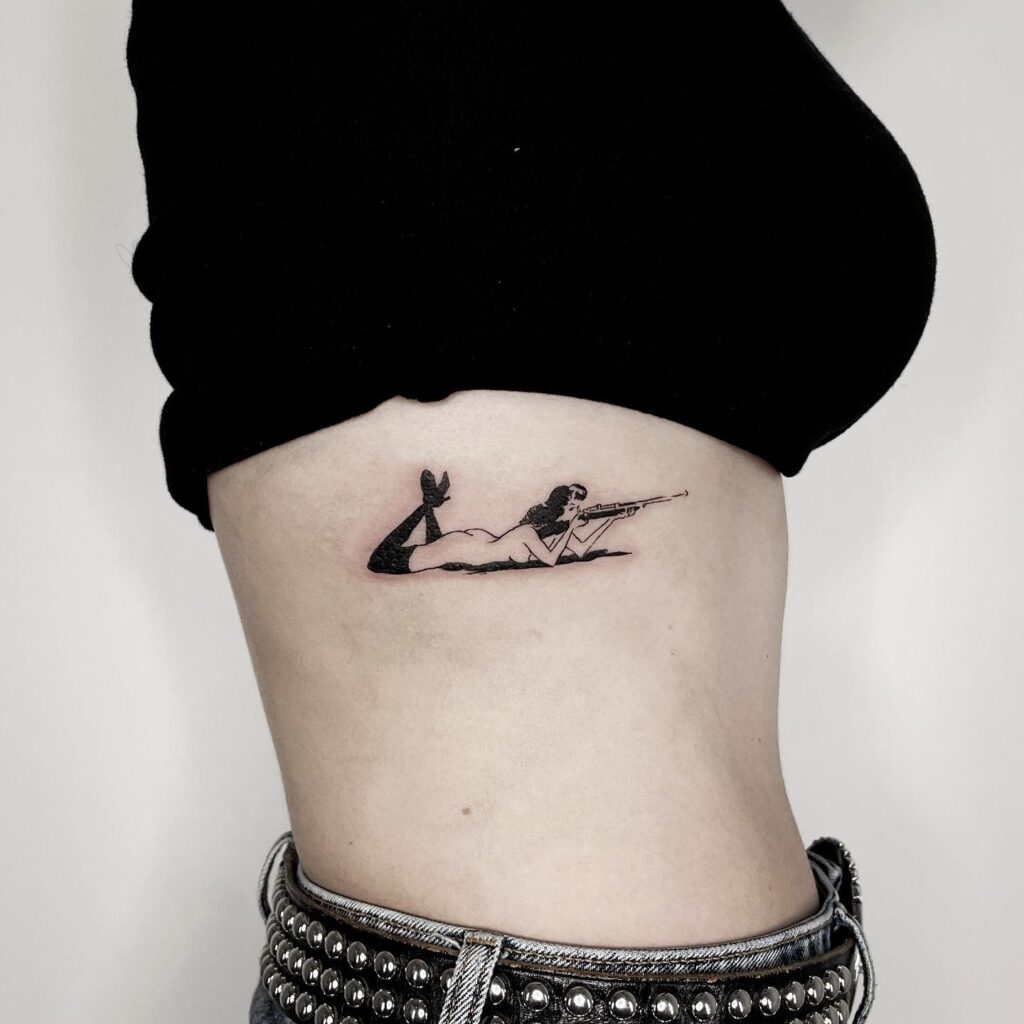 Women with gun shooting black work tattoo on the rib prone shooting position ink