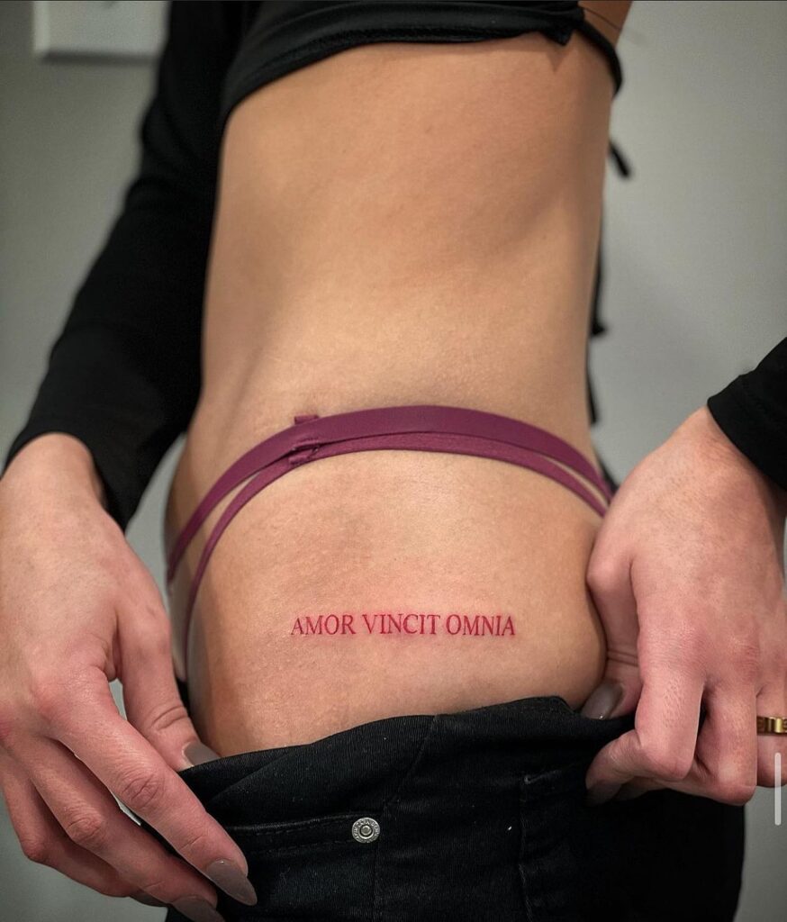 'AMOR VINCIT OMNIA' Red Text Lettering Hip Tattoo for Females, a Passionate Motto: Love Conquers All