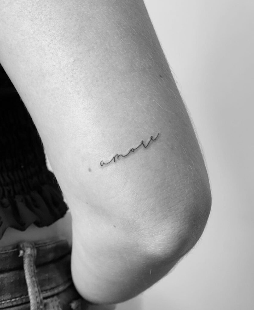 'amore' script lettering tattoo on the back of the arm above elbow, a timeless expression: Amore eterno