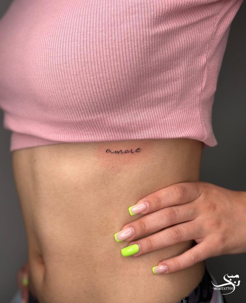 'amore' small script lettering tattoo on the rib subtle and romantic script ink