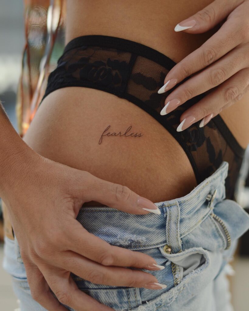'Fearless' Fineline Text Script Lettering Tattoo on the Hip, a Bold Proclamation: Fearless Expression