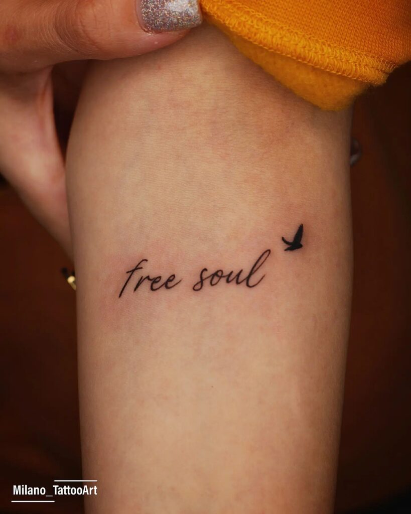 'Free Soul' Fineline Text with Small Black Bird Tattoo on the Forearm: Soulful Freedom