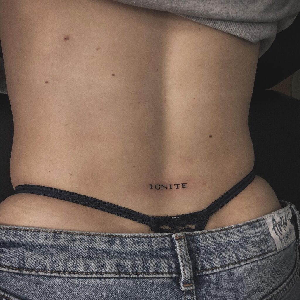 'IGNITE' Text Lettering Tattoo on the Lower Back: Ignite Boldly