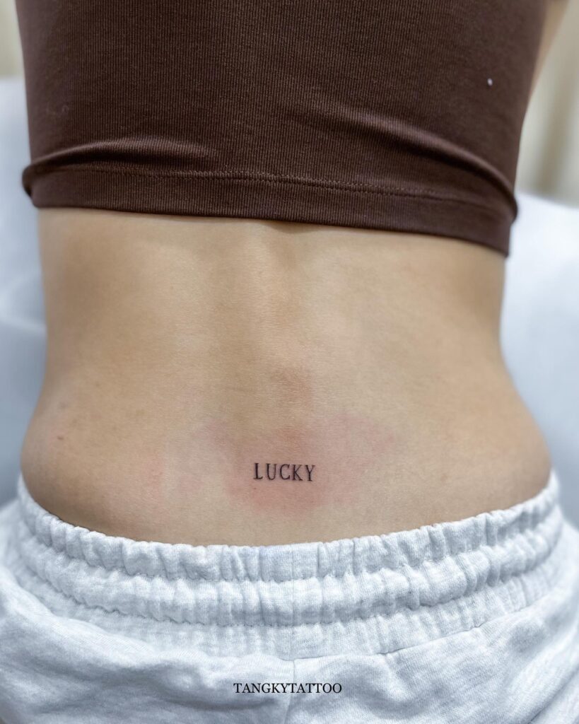 'LUCKY' Text Lettering Tattoo on the Lower Back: Lucky Charms