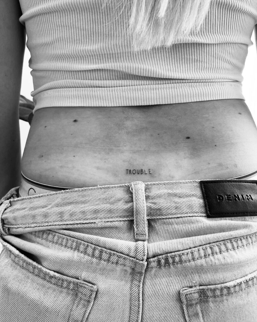 'TROUBLE' Text Lettering Tattoo on the Lower Back: Rebel Spirit